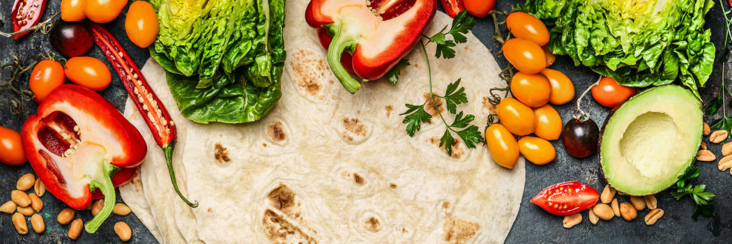 Flat tortillas and various vegetables for burrito making on a table