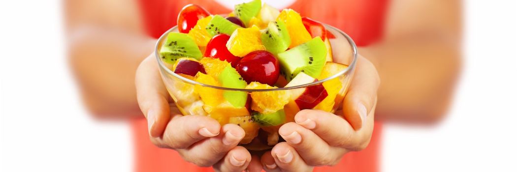 close up of a woman's hands holding out a bowl of colorful fruits