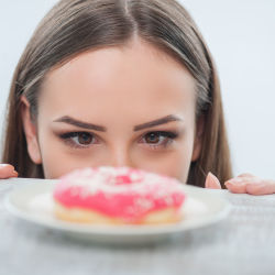 girl looking at unhealthy donut with appetite on a table. Isolated on a white background