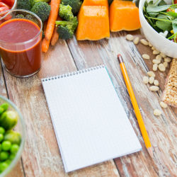 A blank notebook with a pencil surrounded by vegetables