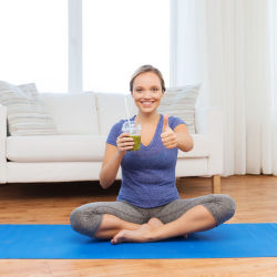 Woman on a yoga mat holding a green smoothie giving a thumbs up