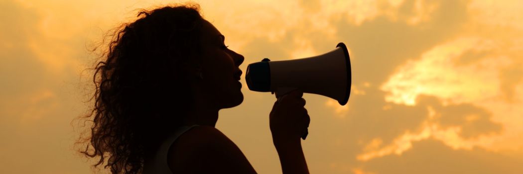 woman's silouette holding a megaphone making a proclamation in front of a sunset sky