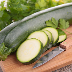 A green zucchini on a cutting board with a few slices next to a sharp knife