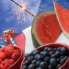 raspberries, blueberries, and watermelon on a table with noise makers and a sparkler for a 4th of July celebration