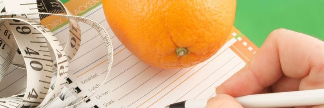 an orange and measuring tape on a journal for weight loss